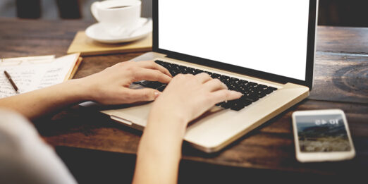 hands typing on a laptop at a dark wooden desk