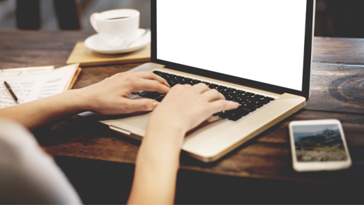 hands typing on a laptop at a brown wooden desk