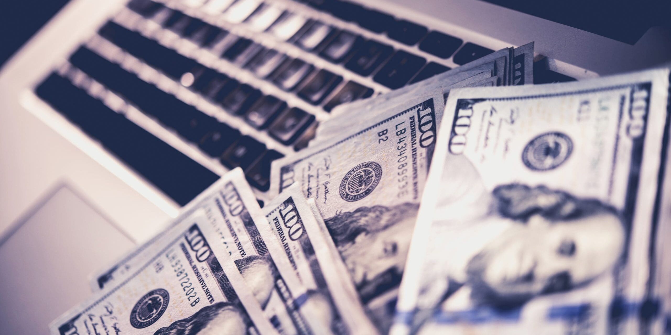 Computer with money hundred dollar bills in front of a laptop