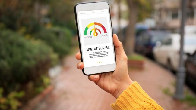 hand wearing a yellow sweater holding a phone with a credit score gauge