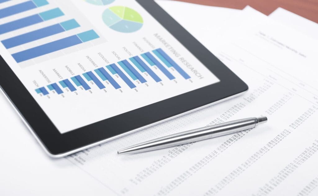 A digital tablet showing data charts next to a silver pen and financial documents on a desk.
