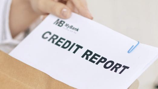 Close-up of a person holding an envelope containing a printed credit report.