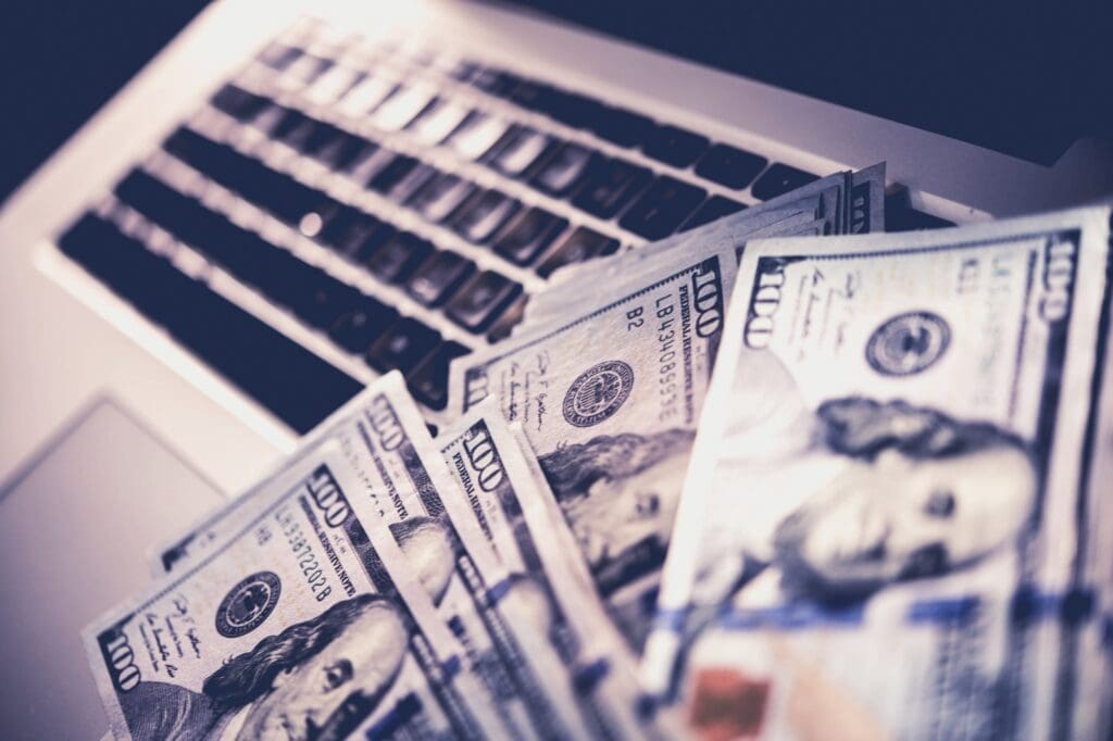 Several US hundred-dollar bills fanned out over a laptop keyboard, representing digital financial collections and AI-driven banking.